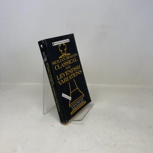 May include: A black book titled "Sicilian Dragon: Classical and Levenfish Variations" with gold lettering and a chess-themed graphic. The book is displayed on a clear acrylic stand.