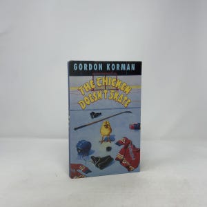 May include: A hardcover book titled "The Chicken Doesn't Skate" by Gordon Korman. The cover features a yellow chick on an ice rink with hockey equipment. The book's spine is dark blue.