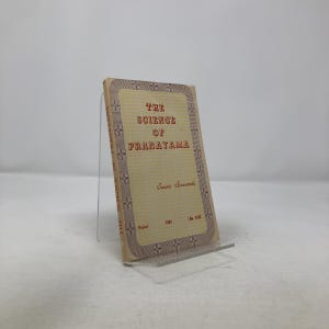 May include: A vintage book titled "The Science of Pranayama" by Swami Sivananda. The book has a beige cover with red text and decorative borders. The book is displayed on a clear acrylic stand.