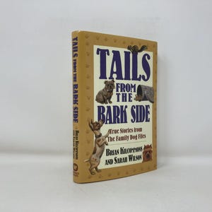 May include: A hardcover book titled "Tails From The Bark Side" with illustrations of dogs and a squirrel. The book has a tan cover with purple lettering and is a collection of true stories from The Family Dog Files.