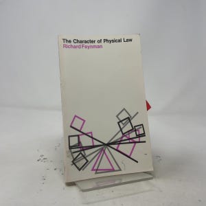 May include: A paperback book titled The Character of Physical Law by Richard Feynman. The white cover features a geometric design with black and magenta lines forming squares and triangles arranged in a symmetrical pattern across the bottom half.