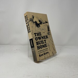 May include: A paperback book titled The Owner Built Home by Ken Kern. The cover is beige with black text and a black and white illustration of a person working on a roof. The spine is black with white text. The book is standing upright.