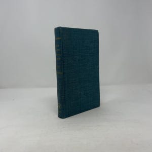 以下が含まれることがあります： ティール色の表紙と金色の文字が入ったハードカバーの本。本の背表紙には、タイトルと著者の名前が金色で表示されています。本は白い背景に立っています。本の表紙は、テクスチャ加工が施されています。