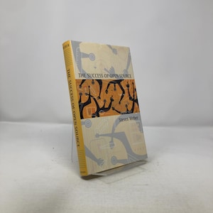 May include: A hardcover book titled "The Success of Open Source" by Steven Weber. The book has a yellow spine with the title printed vertically. The cover features a design of black figures on an orange background.