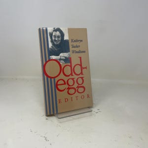 May include: A white ceramic mug with a black handle and the text "But First, Coffee" in a bold, black font. The mug is set against a blurred background, suggesting a cozy setting.