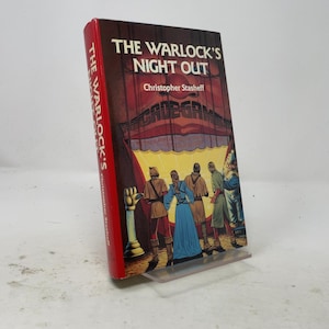 May include: A hardcover book titled The Warlock's Night Out by Christopher Stasheff. The cover features a red spine and a dark illustration of four figures standing before a large, glowing, mouth-like structure with the text Arcade Game above it.