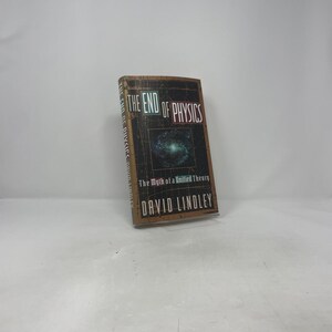 May include: A hardcover book titled "The End of Physics" by David Lindley. The cover features a dark background with the title in large, bold letters and a graphic of a galaxy. The book is standing upright on a white surface.