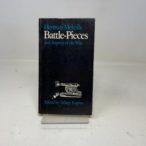 以下が含まれることがあります： ハーマン・メルヴィルの「Battle-Pieces and Aspects of the War」というタイトルのハードカバー本。濃い青色の表紙に白と青の文字が書かれています。表紙には大砲のイラストが描かれています。シドニー・カプラン編。