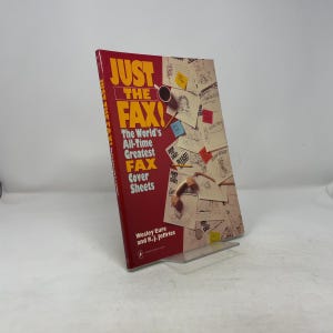 May include: A hardcover book titled "JUST THE FAX!" with a red cover and yellow text. The book features the text "The World's All-Time Greatest FAX Cover Sheets." The book is propped up on a clear stand.