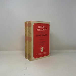 May include: A hardcover book titled The History of Tom Jones, Volume One by Henry Fielding. The cover is red with white text and a small white silhouette portrait. The spine is cream-colored with black text. It is part of the Wesleyan Edition.