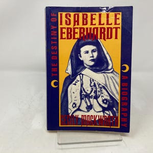 May include: A blue and yellow book cover with the title "The Destiny of Isabelle Eberhardt: A Biography" and a portrait of a woman wearing a blue and white robe.