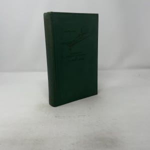 May include: A vintage, dark green book titled "Standard's Aviation Dictionary and Instructor's Guide." The cover features an illustration of an airplane. The book is standing upright on a white surface.
