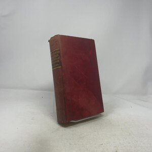 May include: A well-worn, vintage book with a deep red cover. The spine features gold lettering and a small label with the title and author. The book shows signs of age and use, with a slightly faded appearance.