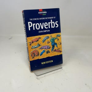 Peut inclure: Un livre à couverture rigide intitulé "The Concise Oxford Dictionary of Proverbs" de John Simpson. La couverture est bleu foncé avec le titre en grandes lettres blanches. La couverture présente également une illustration colorée.