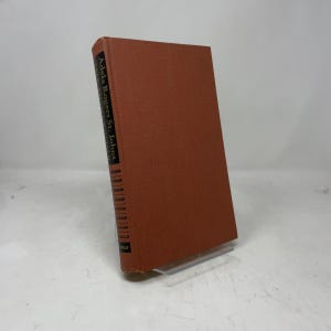 Può includere: Un libro con copertina rigida marrone rossiccio. Il titolo "Adela Rogers St. Johns" è visibile in bianco sul dorso. Il libro è esposto su un supporto trasparente.