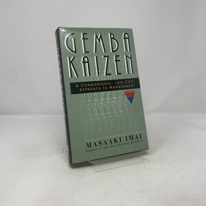 Puede incluir: Un libro de tapa dura titulado "GEMBA KAIZEN" de Masaaki Imai. El libro tiene una cubierta verde con texto blanco y un patrón plateado. El subtítulo dice "A Commonsense, Low-Cost Approach to Management."