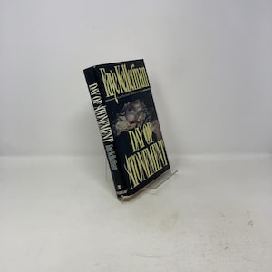 May include: A hardcover book titled "Day of Atonement" by Faye Kellerman. The book has a black cover with white and yellow text. The cover features an illustration of a person's face. The book is displayed on a clear stand.