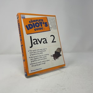 May include: A softcover instructional book titled The Complete Idiot's Guide to Java 2 by Michael Morrison. The cover is white with orange accents, featuring a graphic of coffee beans spilling from a bag and text detailing programming skills.