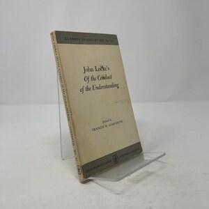 May include: A vintage book titled "John Locke's Of the Conduct of the Understanding" is propped up on a clear stand. The book has a cream-coloured cover with black text and the words "CLASSICS IN EDUCATION" at the top.
