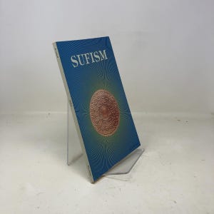 Peut inclure: Un livre intitulé "SUFISM" est présenté sur un présentoir en acrylique transparent. La couverture est bleue avec un motif circulaire central dans des tons marron et or. Le livre est incliné, montrant le titre et le motif.
