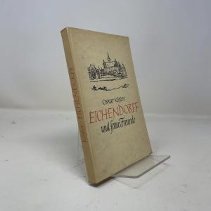 May include: A beige hardcover book titled Eichendorff und seine Freunde by Oskar Köhler. The front cover features a black ink illustration of a castle and town skyline, with the title printed in red and black serif and script lettering.