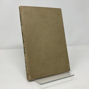 Puede incluir: Un libro antiguo de tapa dura con una cubierta de color beige, apoyado en un soporte de acrílico transparente. El lomo del libro muestra texto descolorido. La cubierta tiene un aspecto ligeramente desgastado, lo que sugiere edad y uso.