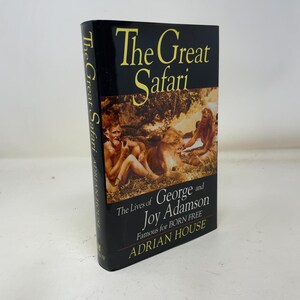 May include: A hardcover book titled The Great Safari: The Lives of George and Joy Adamson by Adrian House. The black dust jacket features yellow text and a central photograph of a man and a woman sitting outdoors with a lion in the grass.