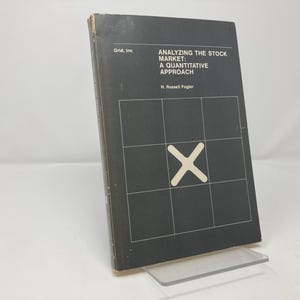 May include: A hardcover book titled "ANALYZING THE STOCK MARKET: A QUANTITATIVE APPROACH" by H. Russell Fogler. The book has a dark gray cover with a grid pattern and a large white "X" in the center. The book is displayed on a clear stand.