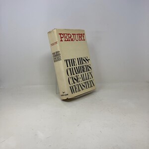 Puede incluir: Un libro de tapa dura titulado "PERJURY" con el subtítulo "THE HISS-CHAMBERS CASE-ALLEN WEINSTEIN". El libro tiene una cubierta de color crema con texto negro y rojo. El libro está ligeramente inclinado, mostrando el título y el autor.