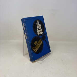 May include: A blue book titled "The Film Sense" by Sergei Eisenstein. The cover displays the title in a white, circular design with a film camera illustration. The author's name is in a similar circular design below.