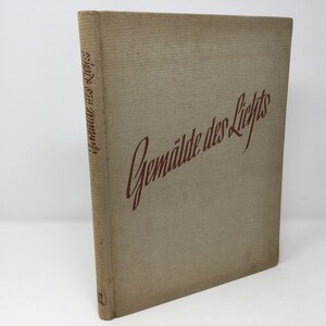 May include: A tan book with the title "Gemälde des Lichts" written in red cursive on the front cover.