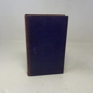 May include: A hardcover book with a dark blue cover and a brown spine. The book is standing upright, showcasing its rectangular shape and the contrast between the cover and spine. The edges of the pages are visible.