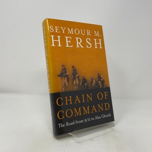 May include: A hardcover book titled Chain of Command: The Road from 9/11 to Abu Ghraib by Seymour M. Hersh. The cover features a bright orange upper section with white text and a dark lower section with an illustration of soldiers in uniform.
