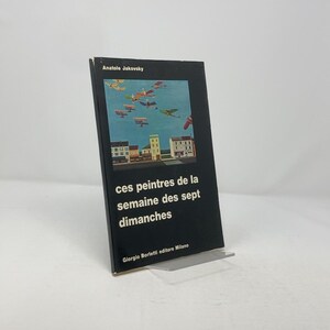 May include: A black book cover with the title "ces peintres de la semaine des sept dimanches" by Anatole Jakovsky. The cover features a colorful illustration of a town with airplanes flying overhead.