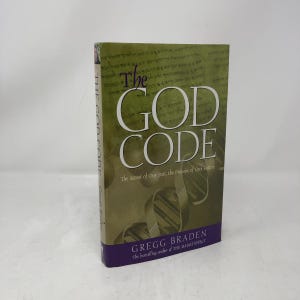 May include: A hardcover book titled "The GOD CODE" by Gregg Braden. The cover features large white text on a green and brown background with a purple band at the bottom. The book's subtitle is "The Secret of Our Past, the Promise of Our Future."