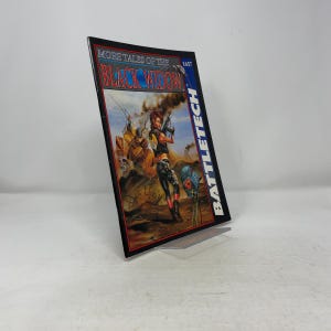Puede incluir: Un libro de bolsillo titulado "More Tales of the Black Widow" con el número 1657. La portada presenta a una mujer con un arma y una armadura futurista. La palabra "BATTLETECH" está impresa verticalmente en el lado derecho del libro.