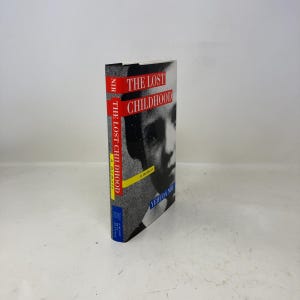 May include: A hardcover book titled "The Lost Childhood" with a black and white portrait on the cover. The title is in red, and the author's name is at the bottom. The spine features the title and author's name in red and yellow.