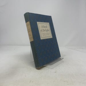 May include: A hardcover book titled "A Book of Delights" with a blue cover featuring a repeating pattern of small gold dots. The book's spine is a darker blue, and the title is in a white box on the cover.