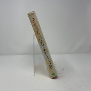 May include: A book titled Newton's Clock: Chaos in the Solar System by Peterson, published by Freeman. The book has a light-colored spine with black text and is displayed standing upright on a clear acrylic stand against a plain background.