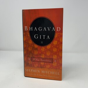 Peut inclure: Un livre intitulé Bhagavad Gita, A New Translation par Stephen Mitchell. La couverture est orange avec un motif répétitif de petits oiseaux dorés. Un grand cercle noir est centré sur le devant avec le titre en lettres blanches à empattement.