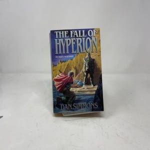 May include: A white ceramic mug with a black handle and the text "But First, Coffee" in a bold, black font. The mug is set against a blurred background, suggesting a cozy setting.