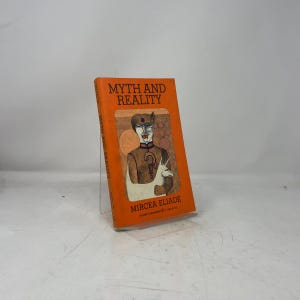 May include: A paperback book titled Myth and Reality by Mircea Eliade with a bright orange cover. The cover features a central illustration of a stylized figure with a question mark on their chest, standing next to a white unicorn-like creature.