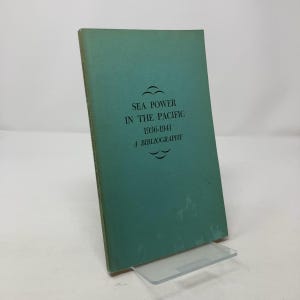 Pode incluir: Um livro verde-azulado com o título "Sea Power in the Pacific 1936-1941 A Bibliography" impresso em preto.