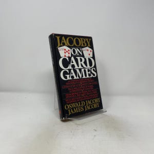 May include: A hardcover book titled Jacoby on Card Games by Oswald Jacoby and James Jacoby. The black cover features gold and white text, with illustrations of playing cards at the top. The book provides instructions for over 150 card games.