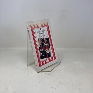 May include: A paperback book titled "Murmuring Judges" by David Hare. The book cover features a photograph of two people in red and white robes. The cover has a red and white geometric border.