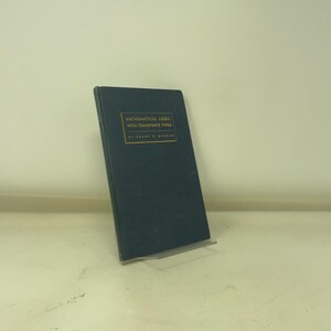 May include: A dark blue book titled "MATHEMATICAL LOGIC WITH TRANSFINITE TYPES" by Frank G. Steiner. The book is propped up on a clear metal stand against a white background. The text is in gold.
