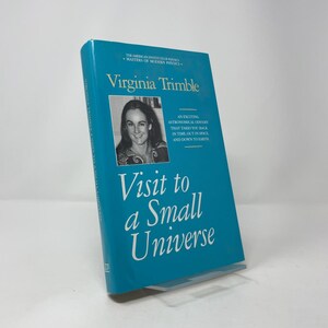 Può includere: Un libro turchese intitolato "Visit to a Small Universe" di Virginia Trimble. La copertina presenta una foto in bianco e nero di una donna e il testo "An exciting astronomical odyssey that takes you back in time, out in space, and down to earth."