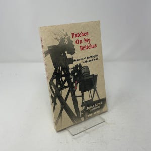 May include: A softcover book titled Patches On My Britches: Memories of growing up in the dust bowl by James Alfred Davidson. The cover features a sepia-toned illustration of a windmill and a barrel on a cart against a light tan background.