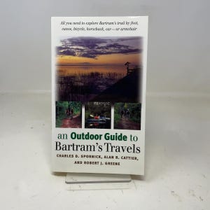 May include: A paperback book titled "an Outdoor Guide to Bartram's Travels." The cover features a sunset over a body of water and three smaller images of outdoor activities. The text reads "All you need to explore Bartram's trail by foot, canoe, bicycle, horseback, car—or armchair."