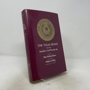 Peut inclure: Un livre relié intitulé The Texas Senate Volume I Republic to Civil War, 1836-1861, édité par Patsy McDonald Spaw. La couverture est bordeaux foncé avec un emblème circulaire doré représentant une étoile et une couronne, et du texte en blanc et or.